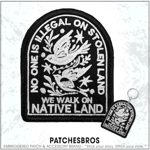 May include: Black embroidered patch with white text and bird design. The patch reads "NO ONE IS ILLEGAL ON STOLEN LAND" and "WE WALK ON NATIVE LAND." A matching keychain is also visible.
