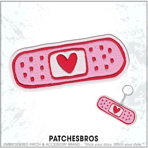 May include: A pink embroidered patch and keychain set shaped like a bandage, featuring a red heart in the center. The patch and keychain have a white border and small red dots. The brand name "PATCHESBROS" is at the bottom.
