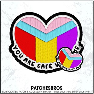 May include: Embroidered heart-shaped patch with a black border and the text "YOU ARE SAFE". The heart is divided into sections of red, yellow, purple, pink, and blue. A smaller heart-shaped keychain is attached.