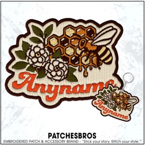 May include: Embroidered patch with a bee, honeycomb, and floral design, with the word "Anyname" in orange script. A matching keychain is also visible. The patch has a brown border and a cream-colored background.