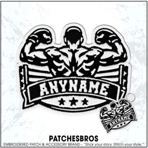 May include: A black and white embroidered patch featuring a muscular boxer with arms raised in a boxing ring. The design includes a banner with the text ANYNAME and three stars below it. A smaller version of the same design is attached to a metal keyring.
