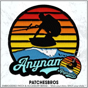 May include: A circular embroidered patch and a matching circular keychain featuring a silhouette of a person wakeboarding against a sunset background of red, orange, and yellow horizontal stripes, with the text Anyname in light blue script.