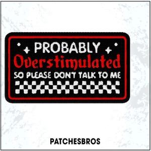 May include: A black rectangular patch with a red border and white embroidered text that reads "PROBABLY Overstimulated SO PLEASE DON'T TALK TO ME." The patch has a checkered pattern at the bottom and two small star-like designs. The brand name "PATCHESBROS" is at the bottom.