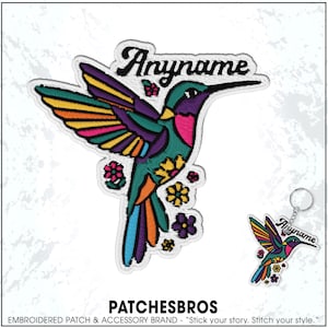 May include: Embroidered patch and keychain featuring a colorful hummingbird design. The hummingbird has a teal body, purple head, and wings with yellow, orange, and purple accents. The text "Anyname" is above the hummingbird.