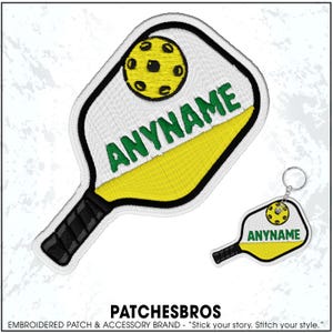 May include: Embroidered pickleball paddle patch and keychain. The patch features a white paddle with a yellow and green design, the text "ANYNAME", and a yellow pickleball. The keychain has a similar design.