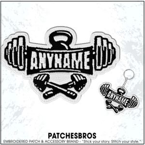May include: Black and white embroidered patch and keychain set featuring a barbell design with the text "ANYNAME". The patch includes a kettlebell and crossed dumbbells. The keychain mirrors the patch design.