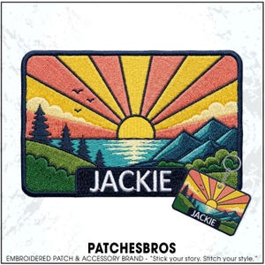 May include: A rectangular embroidered patch and a matching keychain featuring a landscape with a yellow sun, pink and yellow sunrays, blue mountains, green hills, dark blue pine trees, and a blue lake. The name JACKIE is embroidered in white.
