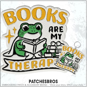 May include: Embroidered patch featuring a green frog reading a book, with the text "BOOKS ARE MY THERAPY" in yellow and black. A matching keychain is also visible. The patch and keychain are white with yellow and green accents.
