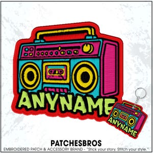 May include: Embroidered patch and keychain featuring a retro boombox design. The patch is outlined in red, with a vibrant color scheme of pink, teal, yellow, and black. The text "ANYNAME" is displayed on the patch.