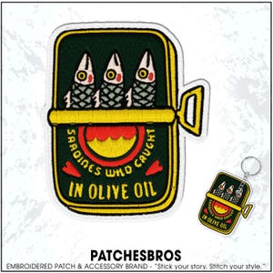May include: Embroidered patch and keychain set featuring a sardine can design. The patch and keychain show three fish inside a can with the text "Sardines Who Caught in Olive Oil". The patch and keychain have a dark green, yellow, red, and white color scheme.