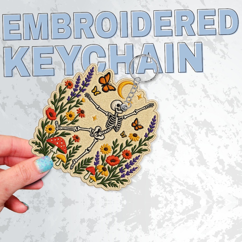 May include: An embroidered keyring featuring a skeleton surrounded by colourful flowers, mushrooms, and butterflies on a beige background. The design includes a yellow crescent moon and is attached to a silver metal ring. The text EMBROIDERED KEYCHAIN is visible in the background.