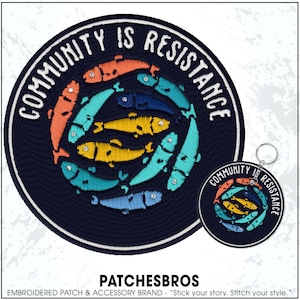 May include: Embroidered patch and keychain featuring a circular design with the text "COMMUNITY IS RESISTANCE." The design includes a ring of colorful fish in orange, teal, yellow, and blue. The patch and keychain are navy blue.