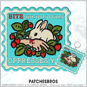 May include: Embroidered patch with a light blue border featuring a white rabbit biting a hand, surrounded by strawberries and green leaves. Text reads "BITE THE HAND THAT OPPRESSES YOU". A matching keychain is also visible.