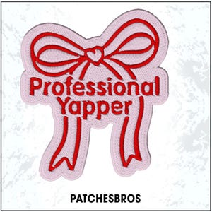 May include: Embroidered patch in the shape of a bow with the words "Professional Yapper" in red thread on a light pink background. The patch also includes the text "PATCHESBROS" at the bottom.