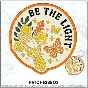 May include: Embroidered patch with the text "BE THE LIGHT" in black, featuring a praying hands design, butterflies, and floral elements in yellow, orange, and green. A matching keychain is also visible.
