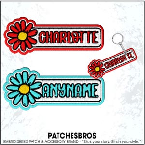 May include: Two rectangular embroidered patches and one matching keychain. One patch features a red daisy with a yellow center and the name CHARLOTTE in red. The other patch features a turquoise daisy with a yellow center and the text ANYNAME.