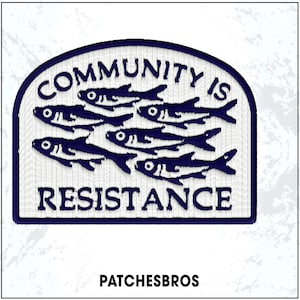 May include: Embroidered patch with a navy blue border and a white background. The patch features the text "COMMUNITY IS RESISTANCE" above a school of stylized navy blue fish. The brand name "PATCHESBROS" is at the bottom.