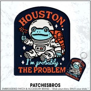May include: Embroidered patch featuring a blue frog astronaut holding flowers, with the text "HOUSTON. I'm probably THE PROBLEM." A matching keychain is also shown. The patch and keychain are navy blue with orange and white details.