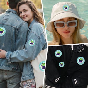 K&ouml;nnte beinhalten: Runde, hellblaue und wei&szlig;e Aufn&auml;her mit einer Cartoon-Froschfigur in einem lila Gewand, die einen Stab h&auml;lt. Die Aufn&auml;her sind auf einer Jeansjacke, einer schwarzen Jacke, einer wei&szlig;en Tragetasche und einem wei&szlig;en Hut abgebildet.