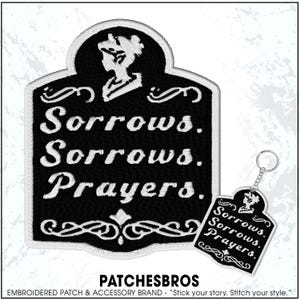 May include: Black and white embroidered patch and keychain set. The patch and keychain feature the words "Sorrows. Sorrows. Prayers." in white script. A silhouette of a woman is at the top of the design.
