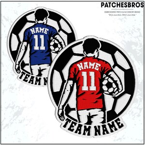 May include: Embroidered patches featuring a soccer player holding a soccer ball, set against a soccer ball design. One patch has a blue jersey with "NAME" and "11", the other has a red jersey with the same details. The text "TEAM NAME" is at the bottom.