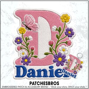 May include: An embroidered patch featuring a large pink letter D decorated with colorful flowers and a pink butterfly. Below the letter, the name Daniel is stitched in blue thread. A smaller matching keychain version is also visible.