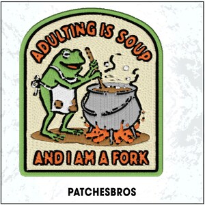 May include: Embroidered patch with a green frog wearing an apron, stirring a pot of soup over flames. Text reads "Adulting is Soup and I am a Fork." The patch has a green border and the brand name "PATCHESBROS" at the bottom.