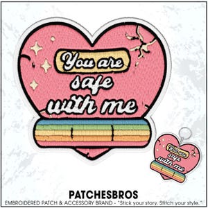 May include: A heart-shaped embroidered patch and matching keychain featuring a pink background, a yellow rectangular banner with the black text You are safe with me, white star accents, and a horizontal rainbow stripe at the bottom edge.