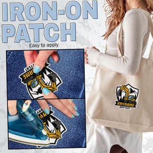 May include: An iron-on patch featuring a yellow excavator graphic inside a shield shape with black mountain silhouettes. The patch includes customisable text areas labelled ANYNAME and ANYTEXT. The image shows the patch being applied to fabric.