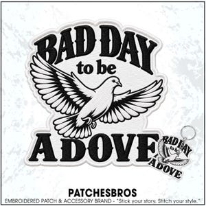May include: An embroidered patch and a matching keychain featuring a white dove in flight with black wings and tail feathers. The text BAD DAY to be A DOVE is stitched in bold black lettering above and below the bird on a white background.