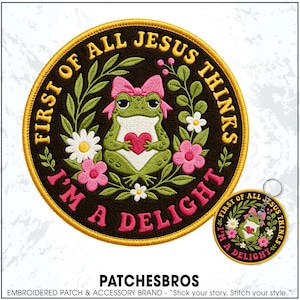 May include: A circular embroidered patch and a matching keychain featuring a green frog with a pink bow holding a red heart. The design includes white and pink flowers, green leaves, and the yellow and pink text: FIRST OF ALL JESUS THINKS I'M A DELIGHT.