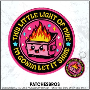 May include: A pink embroidered patch with the text "THIS LITTLE LIGHT OF MINE I'M GONNA LET IT SHINE" encircling a cartoon dumpster on fire. A matching keychain is also visible.
