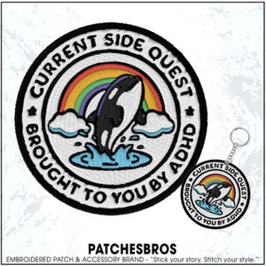 May include: Embroidered patch and keychain featuring a black and white orca leaping through water under a rainbow. The patch and keychain have the text "CURRENT SIDE QUEST BROUGHT TO YOU BY ADHD" in a circular design.