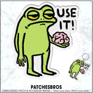 May include: Embroidered patch featuring a cartoon frog with a weary expression, holding a pink brain. The patch has the text "USE IT!" in bold letters. A matching keychain is also visible. The brand name "PATCHESBROS" is at the bottom.