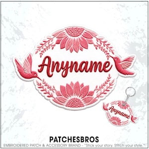 May include: An oval embroidered patch and a matching circular keychain featuring the text Anyname in red script. The design includes pink sunflowers at the top and bottom, flanked by two pink hummingbirds on the sides, all on a white background.