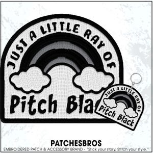 May include: Embroidered patch and keychain set with a black and white rainbow design. The patch and keychain feature the text "JUST A LITTLE RAY OF Pitch Black" and two white clouds. The brand name "PATCHESBROS" is also visible.