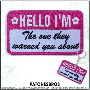 May include: A pink embroidered patch and keychain with the text "HELLO I'M The one they warned you about." The patch and keychain have a white background with a pink border and floral accents.
