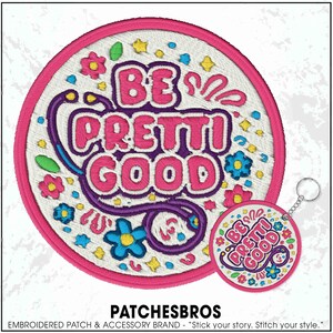 May include: Embroidered patch with the words "BE PRETTI GOOD" in pink and purple. The patch is round with a pink border and features floral and star designs. A matching keychain is also visible.