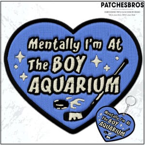May include: Embroidered patch and keychain set. The patch is heart-shaped, light blue with black trim, and features the text "Mentally I'm At The BOY AQUARIUM" in white. Includes hockey stick and puck graphics. The keychain mirrors the patch design.