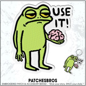 May include: Embroidered patch featuring a green frog with yellow eyes holding a pink brain, with the text "USE IT!". A smaller keychain version is also shown. The brand name "PATCHESBROS" is at the bottom.