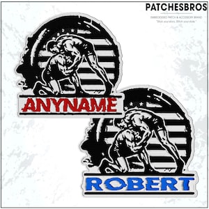 May include: Embroidered patches featuring a wrestling design with a silhouette of two wrestlers in action, set against a black and white American flag background. The patches have a rectangular nameplate with the text "ANYNAME" and "ROBERT". The brand name "PATCHESBROS" is at the top.