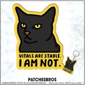 May include: Embroidered patch and keychain set featuring a black cat with yellow accents. The patch and keychain have the text "VITALS ARE STABLE. I AM NOT." The brand name "PATCHESBROS" is at the bottom.
