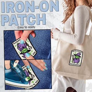 May include: An iron-on patch with a cartoon frog wizard design, with the text "OFF To Commit Tomfoolery". The image also shows the text "IRON-ON PATCH Easy to apply". The patch is being applied to denim.