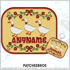 May include: Embroidered patch and keychain featuring three white geese with orange beaks and feet, wearing red neck ribbons, on a yellow background. The word "ANYNAME" is embroidered in red. A red border and floral accents complete the design.