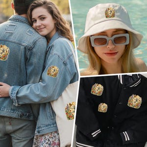 May include: A collection of embroidered patches featuring a skeleton dancing amidst colourful wildflowers, butterflies, and a sun. These patches are displayed on blue denim jackets, a white tote bag, a white bucket hat, and a black bomber jacket.