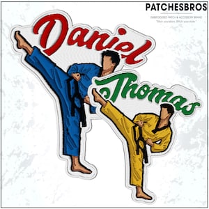 May include: Embroidered patches featuring two martial artists in action. One patch displays the name "Daniel" in red, and the other says "Thomas" in green. Both figures are in a kicking pose, one in a blue uniform and the other in yellow.