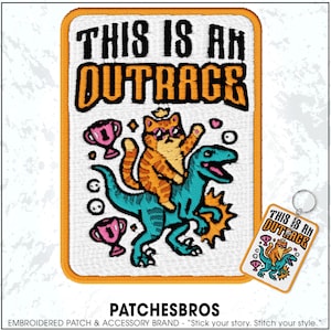 May include: Embroidered patch with the text "THIS IS AN OUTRAGE". The patch features a cartoon cat riding a blue dinosaur, with pink trophies and bubbles. A matching keychain is also visible.