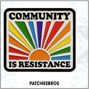 May include: Embroidered patch with the words "COMMUNITY IS RESISTANCE" in black, arched over a rainbow sunburst design. The patch has a black border and a white background. The brand name "PATCHESBROS" is at the bottom.