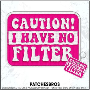 May include: A hot pink embroidered patch with the text "CAUTION! I HAVE NO FILTER" in white. A smaller keychain with the same design hangs from the patch. The patch is rectangular with rounded corners.