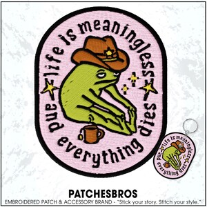 May include: Embroidered patch with a green frog wearing a brown cowboy hat, with the text "and life is meaningless everything dies" in a pink oval. A matching keychain is also visible.